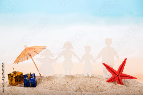 Paper figures joined hands - family, an umbrella, gifts and starfish in the sand against the background of the sea.