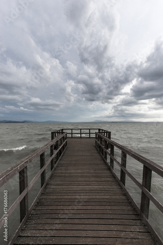 First person view of a pier on a lake on a moody day, with dark water and overcast, stormy sky