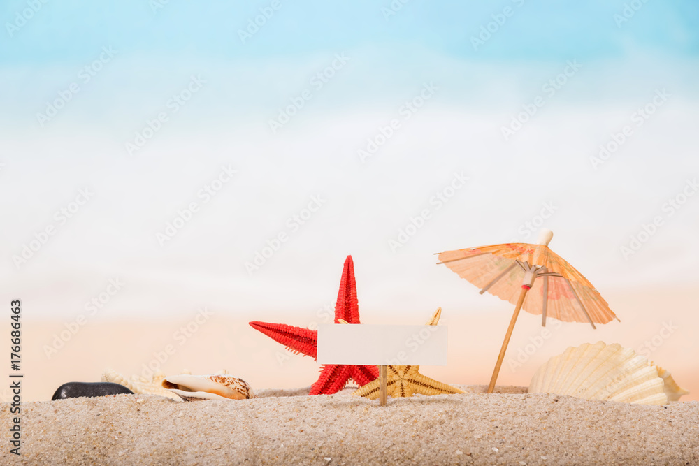 A blank card on peg, starfish, an umbrella, sea shell and shell in the sand against the background of the sea. A blank card on peg, starfish, an umbrella, sea shell and shell in the sand against the background of the sea.