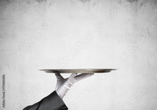 Hand of butler holding empty metal tray against concrete background photo