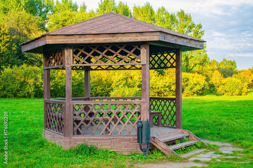 Fototapeta Wooden arbour in park a background of green lawn and trees