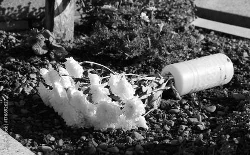 black and white photo of a fallen vase with white flowers on the cemetery