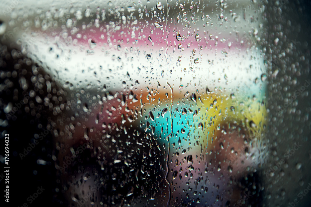 Drops of rain on a window pane, people in background. Shallow depth of field.