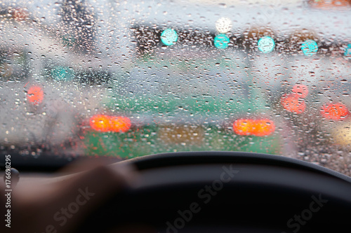 people driving car and water droplet on car mirror or windshield with rain storm and traffic jam on expressway road with red light at behind the car and green traffic light
