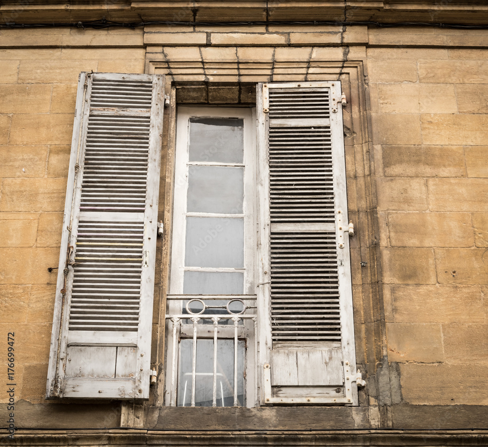 Old windows with weathered shutters in a facade of a kind of mansion with a forged ornamental fence, viewing point is from below. Coloring is somewhat bleak and gray. Style is old French. Old windows with weathered shutters in a facade of a kind of mansion with a forged ornamental fence, viewing point is from below. Coloring is somewhat bleak and gray. Style is old French.