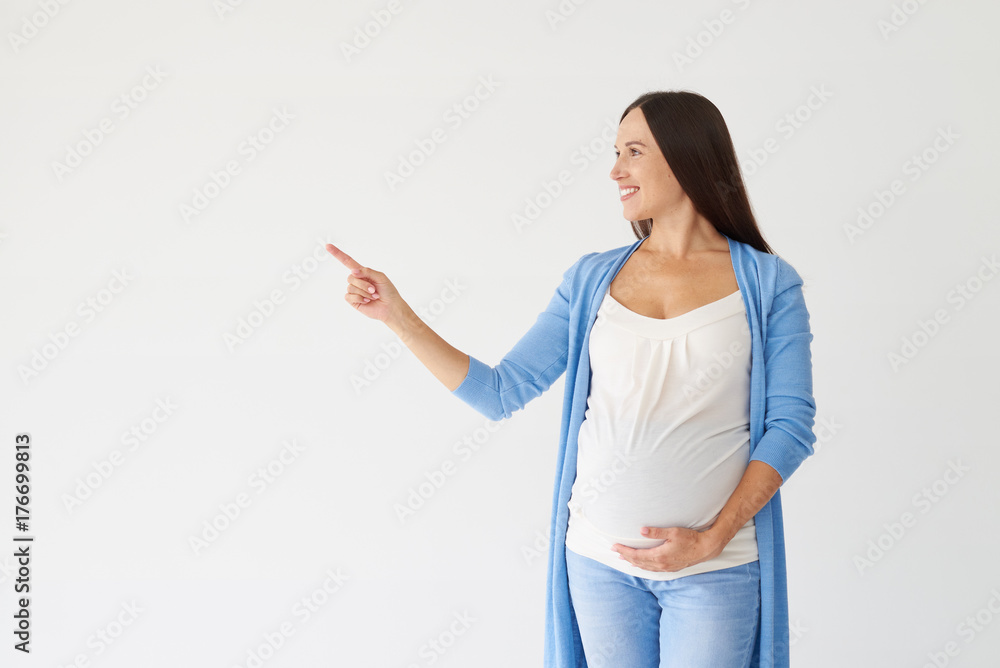 Happy young pregnant woman pointing at copy space in studio Happy young pregnant woman pointing at copy space in studio