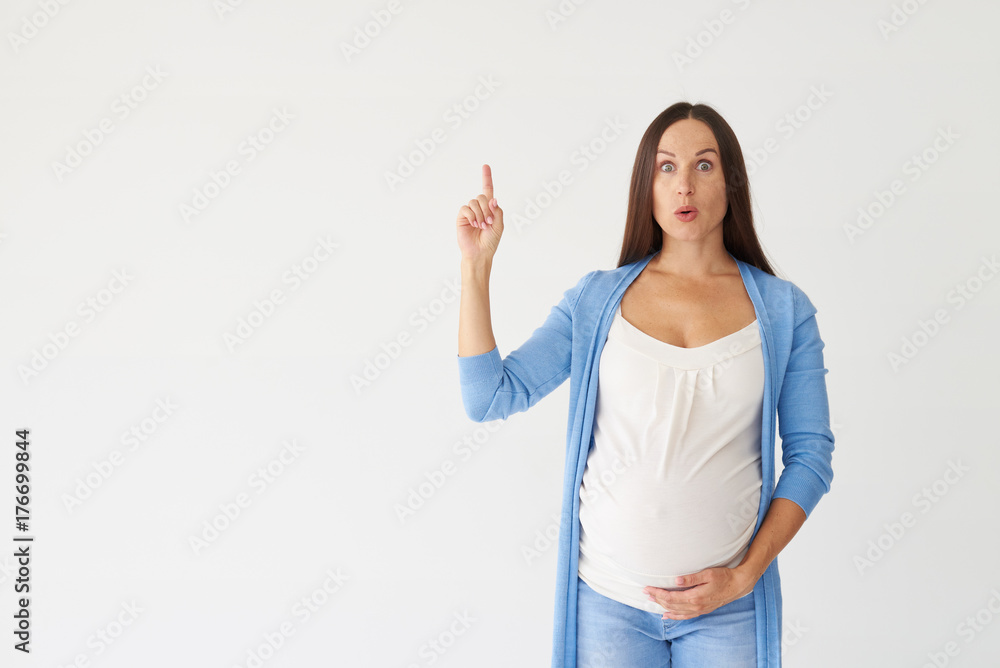Surprised pregnant woman pointing finger up in studio Surprised pregnant woman pointing finger up in studio