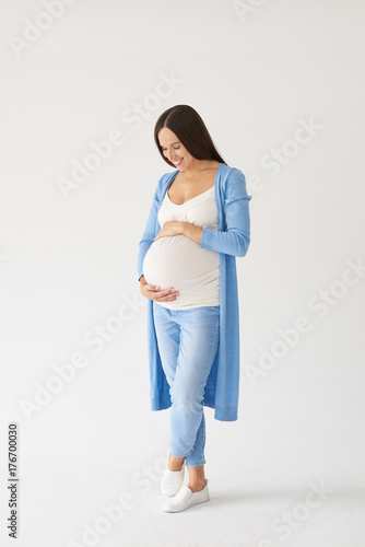 Loving pregnant woman looking at belly while posing in studio