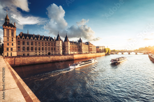 Dramatic sunset over river Seine and Conciergerie in Paris, France, with cruise boats and Pont Neuf. Colourful travel background. Romantic cityscape. © Funny Studio