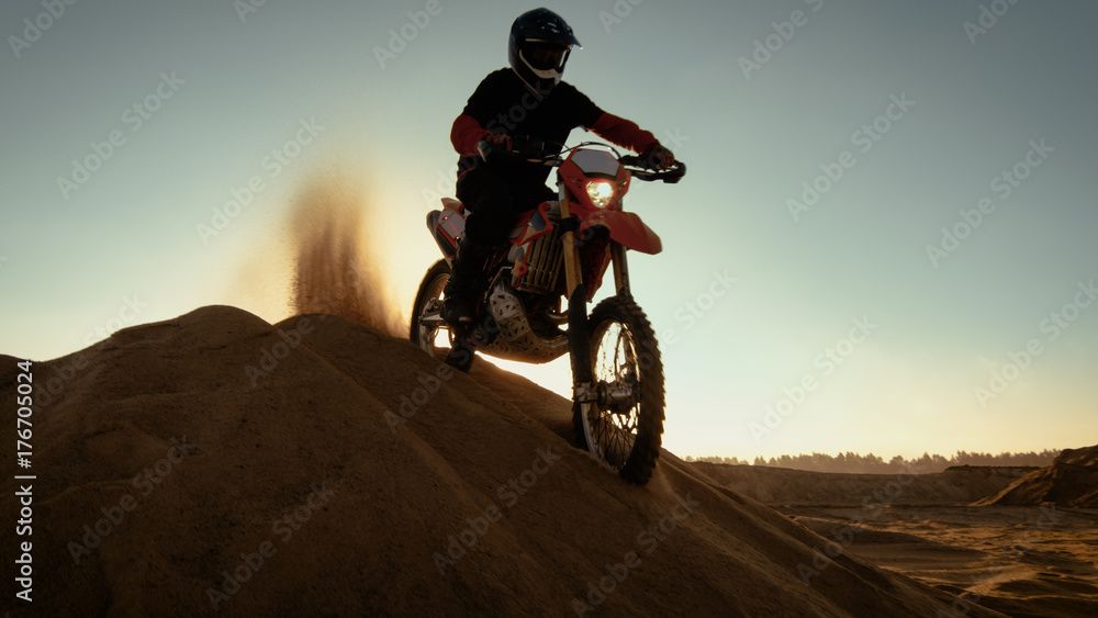 Fototapeta Professional Motocross Rider on FMX Motorcycle Stands on the Sand Dune and Overlooks Off-Road Track, then Drives Down.