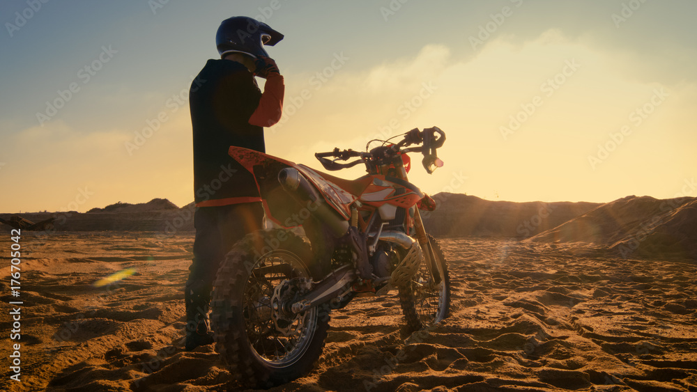 Obraz premium Niskie ujęcie profesjonalnego kierowcy motocrossowego zakładającego kask i przygotowującego się do jazdy na swoim motocrossie.