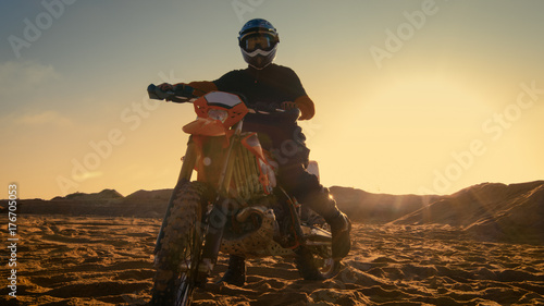 Front View Shot of the Professional Motocross Driver Saddles His FMX Dirt Bike on the Sand/ Dirt Track.