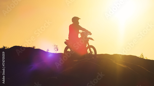 Professional Motocross Rider on FMX Motorcycle Stands on the Sand Dune and Overlooks Extreme Off-Road Terrain that He Gonna Ride Today.
