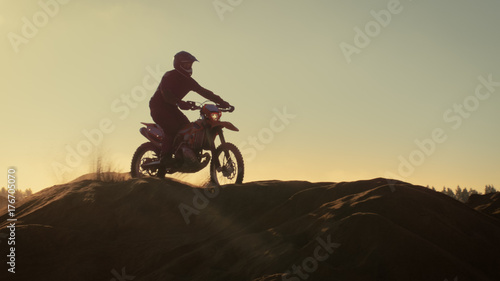 Professional Motocross Motorcycle Rider Drives Over the Dune and Further Down the Off-Road Track. It's Sunset.