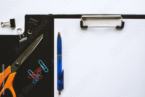 White paper on clipboard with office tool stationery (pen, scissors, binder and paper clips) on white table