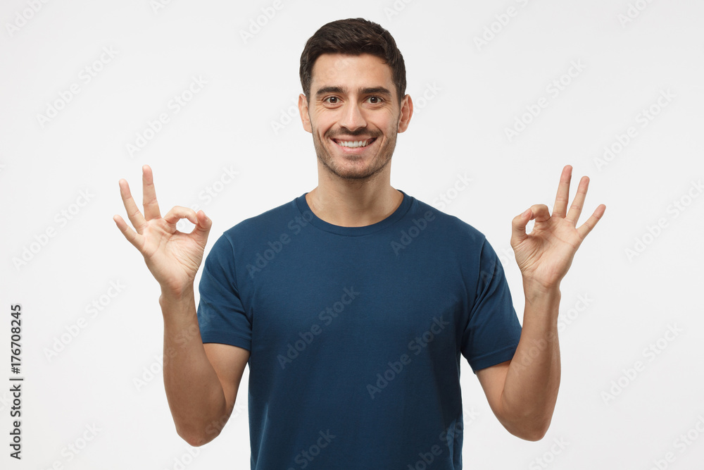 Portrait of good looking man isolated on grey background smiling, and showing okay sign with both hands, sharing positive experience addressing audience with advice Portrait of good looking man isolated on grey background smiling, and showing okay sign with both hands, sharing positive experience addressing audience with advice