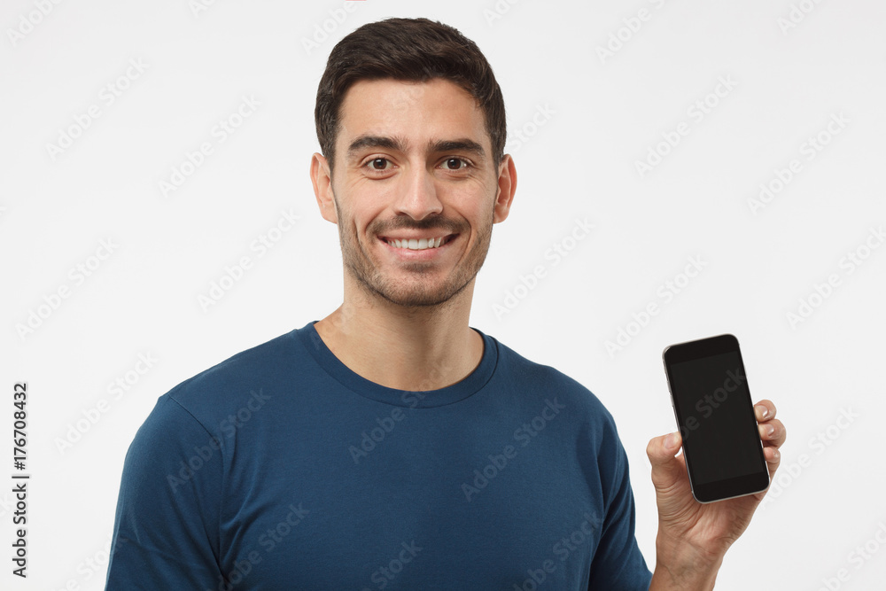 Closeup of young handsome man smiling isolated on grey background, holding and showing blank smartphone with copyspace for advertisement of applications, websites, goods and services Closeup of young handsome man smiling isolated on grey background, holding and showing blank smartphone with copyspace for advertisement of applications, websites, goods and services