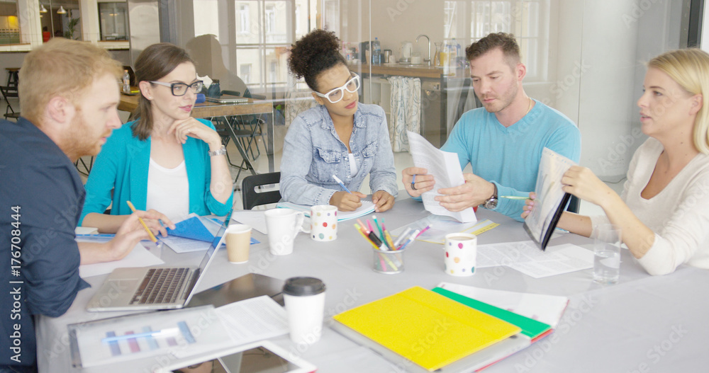 Fototapeta premium Side view of woman holding folder with document and showing it to coworkers while having conference at table in modern office.