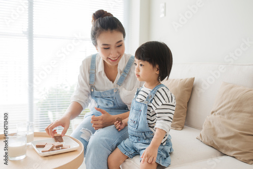 Cute little girl and her beautiful mother drinking milk and eating cookies