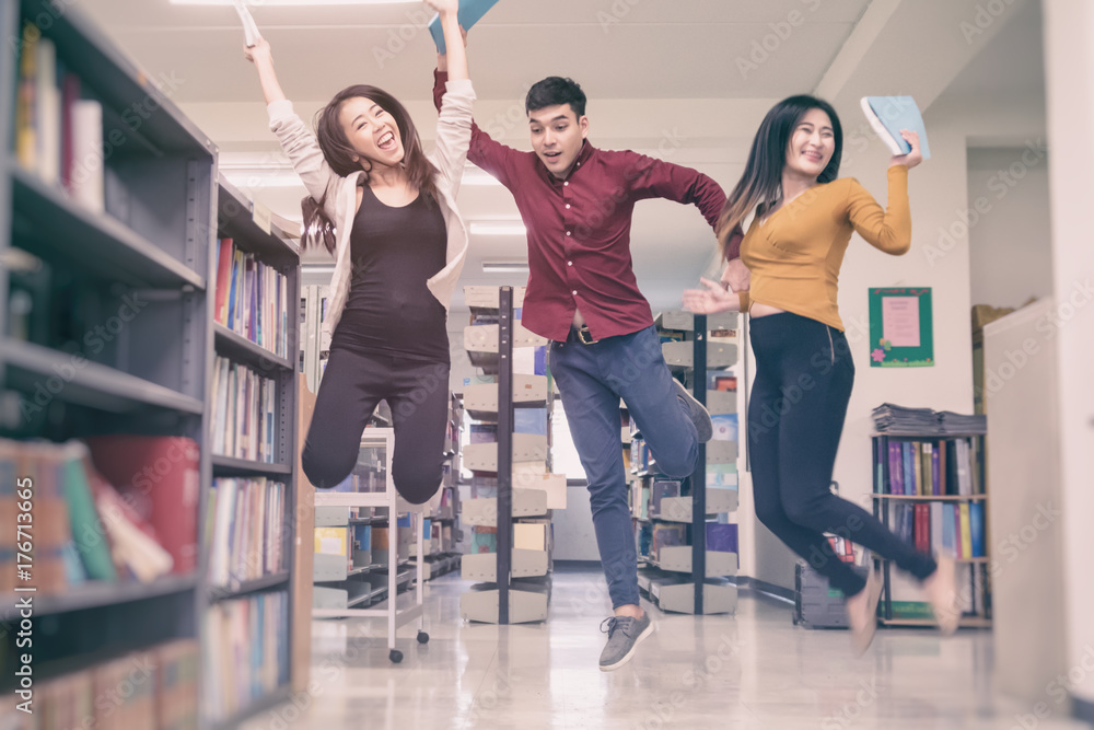 Fototapeta premium Group of student jumping with hand up in University library