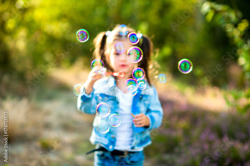little girl walks in the evening park, lets out soap bubbles and has fun