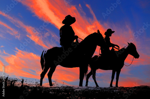 silhouette cowboy and horse on blurry colorful sunset sky. © rathchapon