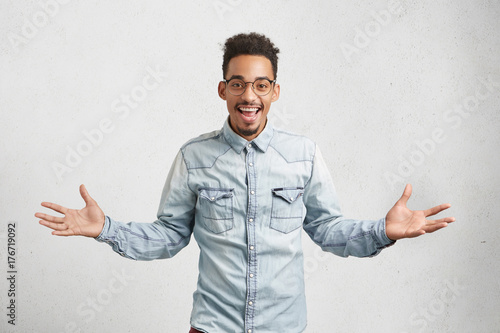 Handsome male with shaggy hairstyle, gestures happily, smiles cheerfully, feels carefree as has day off, decides what to do and how spend it. Excited male student passes successfully all exams photo