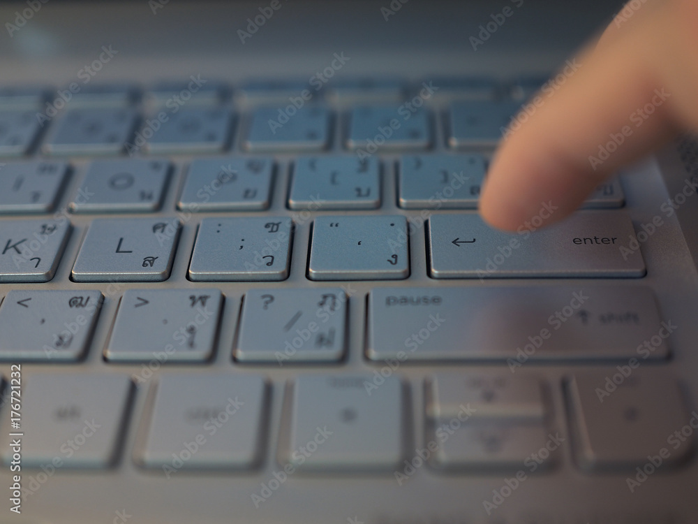 Perspective part of silver aluminum laptop keyboard, with forefinger pressing Enter button, with reflection shadow, English and Thai alphabet letter label version Perspective part of silver aluminum laptop keyboard, with forefinger pressing Enter button, with reflection shadow, English and Thai alphabet letter label version