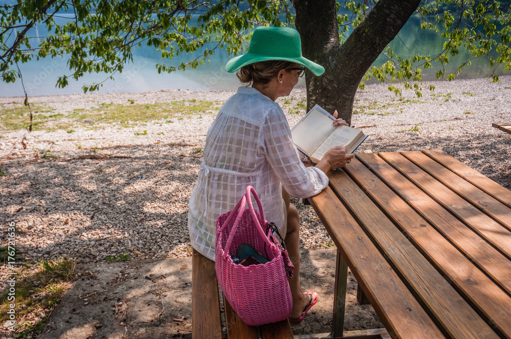 Woman reading book sitting on a table under tree by lake