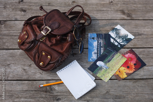Top view of a backpack, sunglasses, photos, a notepad with a pencil on a wooden background