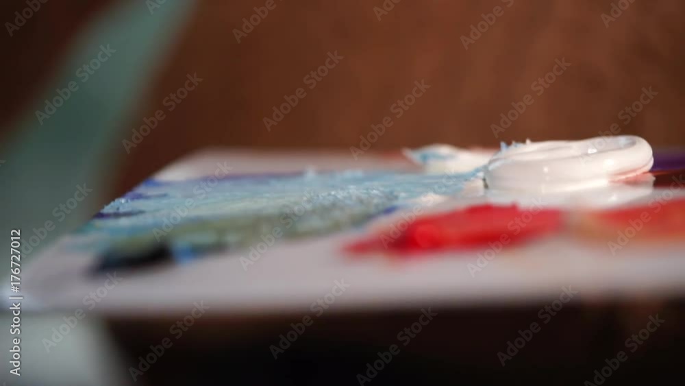 Painter is taking colors by paintbrush from palette-bed, holding in a hand. Close-up shot of details in art workshop during masters work.