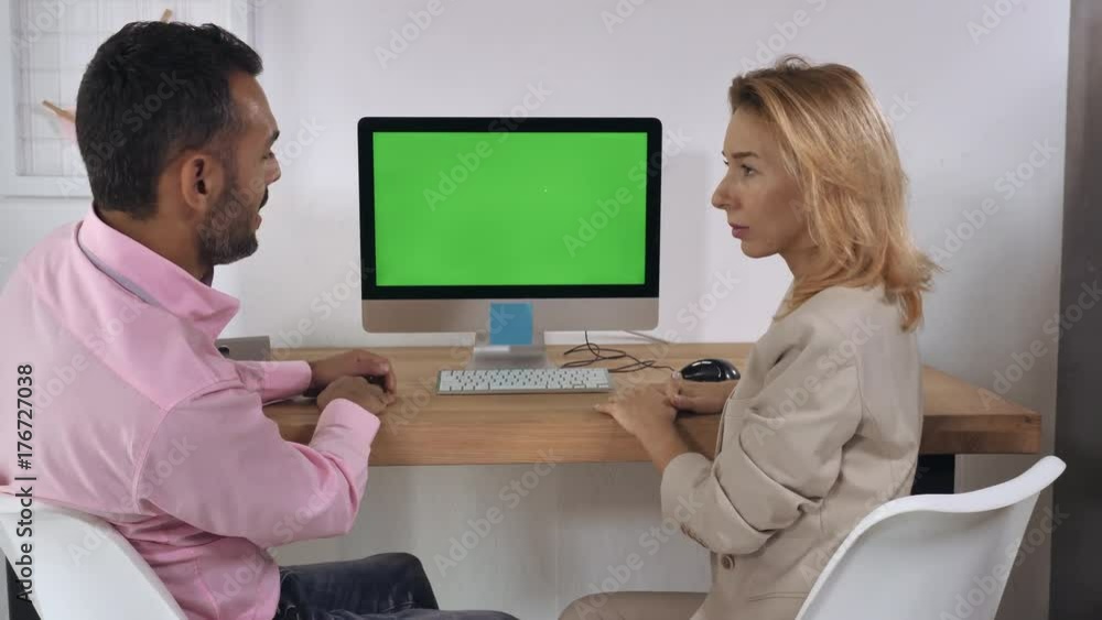 Business people sitting in front of computer with green display talking and looking on screen pc. Adult professional employees discussing presentation before meeting with partners Business people sitting in front of computer with green display talking and looking on screen pc. Adult professional employees discussing presentation before meeting with partners