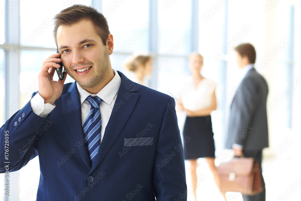 Smiling businessman in office with colleagues in the background Smiling businessman in office with colleagues in the background