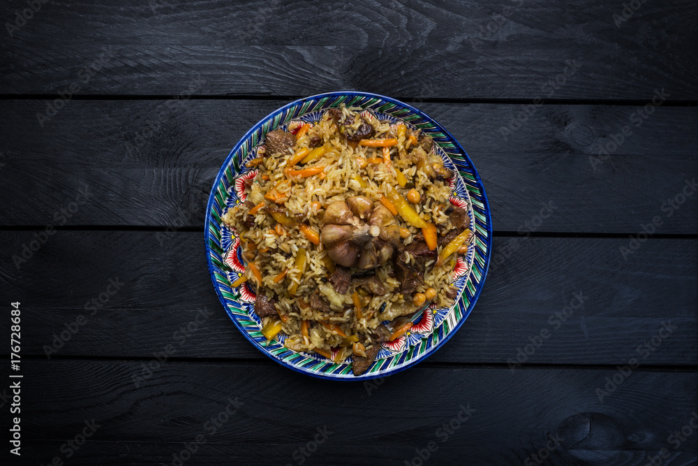 Pilaf on plate with oriental ornament on a wooden background. Central-Asian cuisine - Plov. Top view