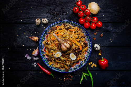 Pilaf and ingredients on plate with oriental ornament on a dark wooden background. Central-Asian cuisine - Plov Top view