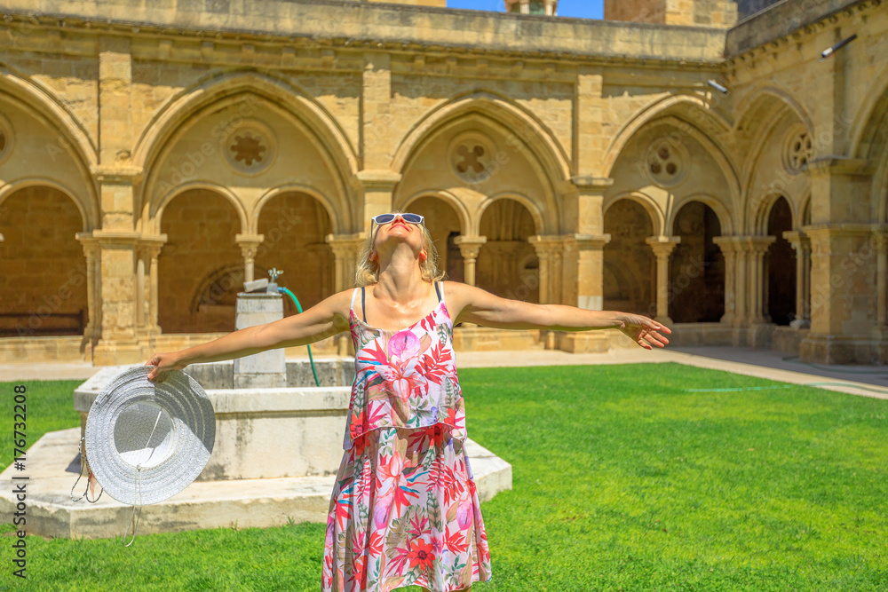 Naklejka premium Freedom woman with open arms at old Coimbra Cathedral cloister. Se Velha de Coimbra is one of most important romanesque buildings in Portugal. Female tourist enjoying in university town of Coimbra.