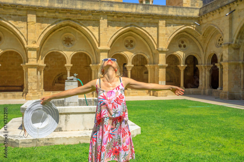 Freedom woman with open arms at old Coimbra Cathedral cloister. Se Velha de Coimbra is one of most important romanesque buildings in Portugal. Female tourist enjoying in university town of Coimbra.