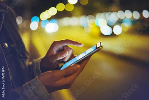 Girl pointing finger on screen smartphone on background illumination glow bokeh light in night atmospheric city, hipster using in hands mobile phone, mockup glitter street , online internet concept