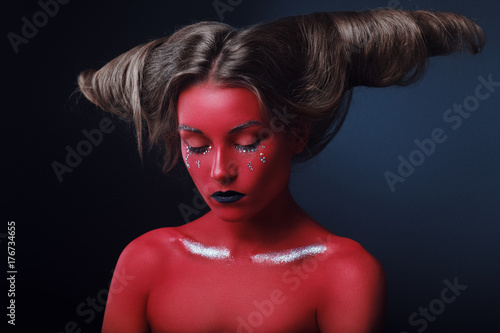 Portrait of a girl in a high fashion, beauty style with red skin, black lips make up at dark background. Devil makeup fashion art design. Halloween holiday concept