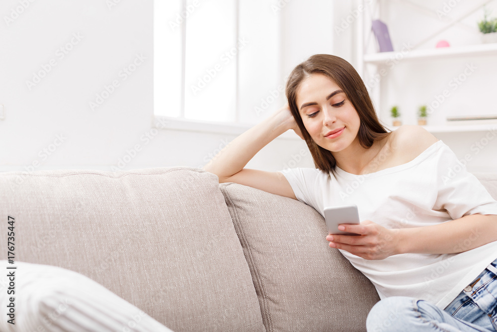 Young brunette woman using smartphone at home on the couch. Dark-haired girl in casual texting online Young brunette woman using smartphone at home on the couch. Dark-haired girl in casual texting online