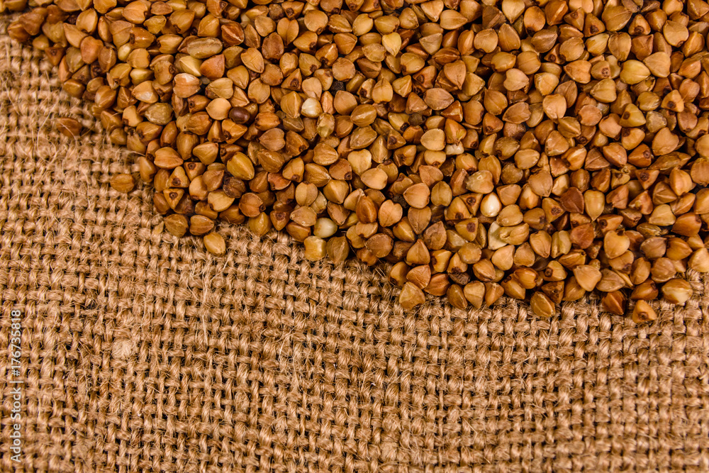 Fototapeta premium Pile of the raw buckwheat on sackcloth. Top view
