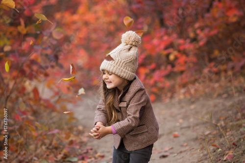 Little girl throw leaves at the autumn