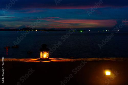 The light or lantern is shining in the dark and placed on the edge of the mortar with sea and twilight sky at night as background.