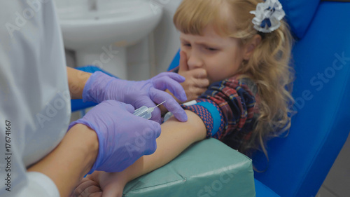 Nurse is taking blood sample from a vein in the arm of little girl
