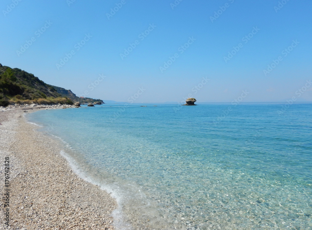 An empty white stone beach with transparent turquoise sea and rocks in Cephalonia or Kefalonia in Greece.