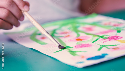 Close-up of a brush in the hand of a child drawing flowers with colorful watercolors. School, education concept.