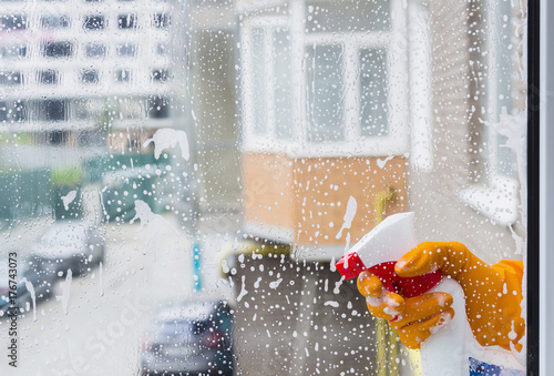 Window cleaning service. Hand with orange rubber glove cleaning window with spray detergent. Image with copy-paste.  photo