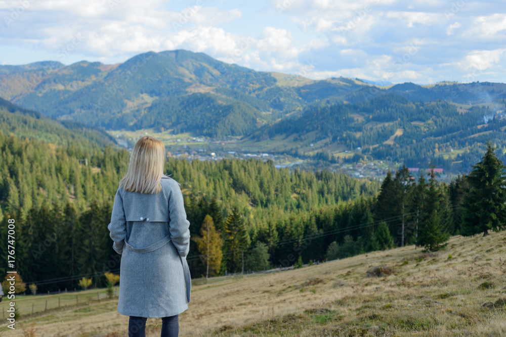 A young blond girl is standing on top and enjoying the panorama of a mountain town.
