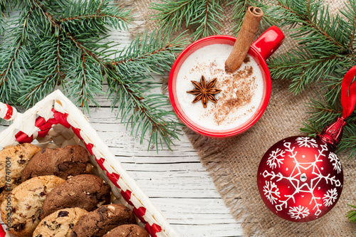 eggnog cocktail in mug arranged with christmas decoration and cookies box on white wooden table