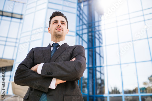 Confident business expert. Thoughtful young businessman holding hand on chin and looking at camera while standing outdoors with office building in the background